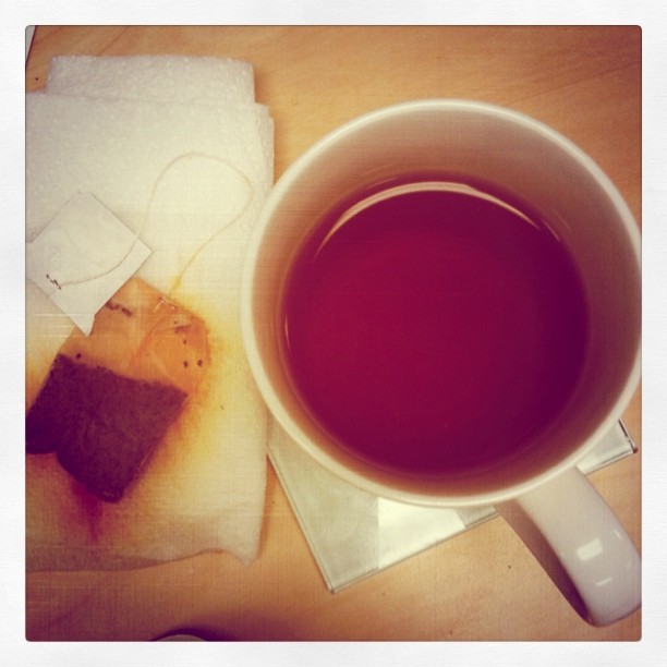 Cup of tea with tea bag on a paper towel next to it.