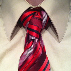 tan shirt with red/orange/black striped tie tied in a cape knot